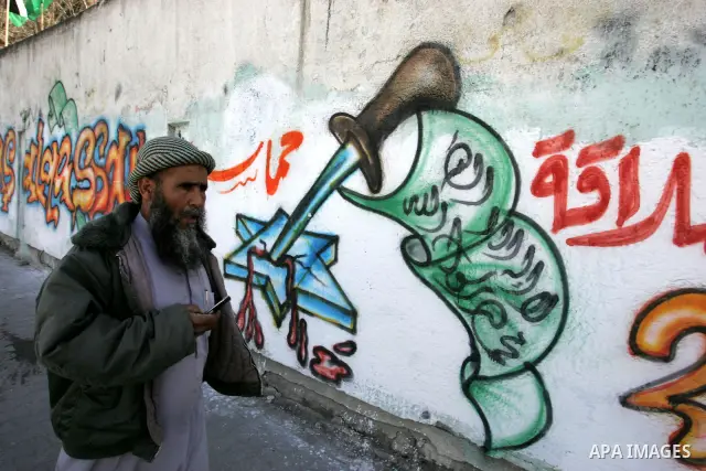 Palestinians walk past murals depicting slogans for Hamas in preparation for the celebrations marking the Islamist movement's 24th anniversary, Rafah refugee camp, in southern Gaza Strip on Dec. 13,2011. The main celebra...