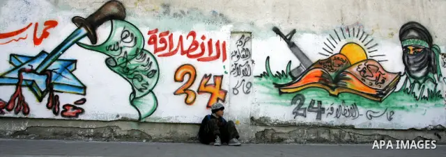 Palestinians walk past murals depicting slogans for Hamas in preparation for the celebrations marking the Islamist movement's 24th anniversary, Rafah refugee camp, in southern Gaza Strip on Dec. 13,2011. The main celebra...