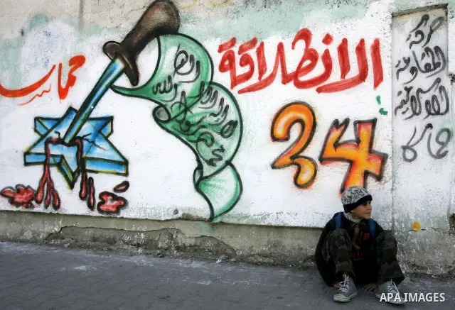 Palestinians walk past murals depicting slogans for Hamas in preparation for the celebrations marking the Islamist movement's 24th anniversary, Rafah refugee camp, in southern Gaza Strip on Dec. 13,2011. The main celebra...