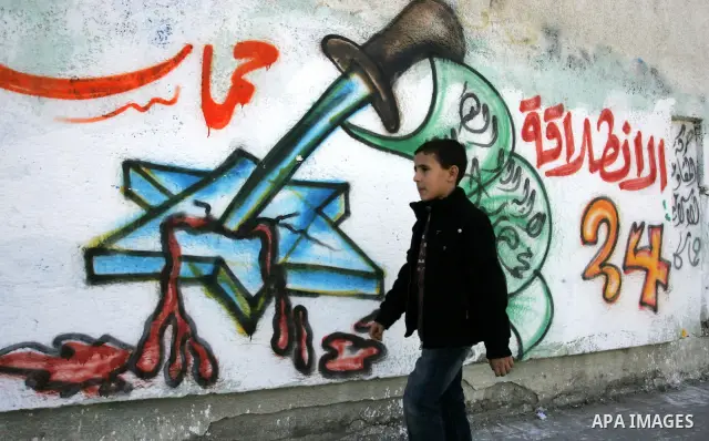 Palestinians walk past murals depicting slogans for Hamas in preparation for the celebrations marking the Islamist movement's 24th anniversary, Rafah refugee camp, in southern Gaza Strip on Dec. 13,2011. The main celebra...