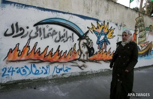 Palestinians walk past murals depicting slogans for Hamas in preparation for the celebrations marking the Islamist movement's 24th anniversary, Rafah refugee camp, in southern Gaza Strip on Dec. 13,2011. The main celebra...
