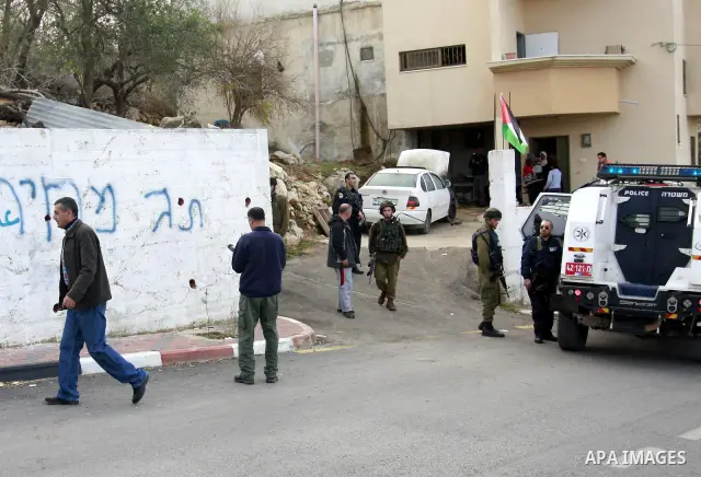 Palestinians and Israeli soldiers stand next a burning vehicle which residents said was torched by Jewish settlers in the West Bank Village of Harith near Nablus, Wednesday , Dec. 12, 2011. leaving behind a graffiti mess...