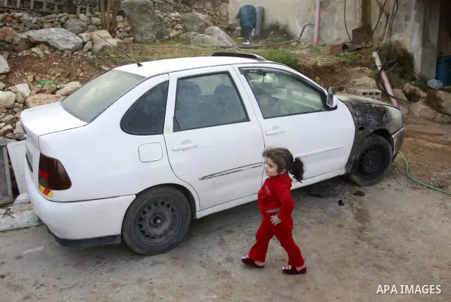 Palestinians stand next a burning vehicle which residents said was torched by Jewish settlers in the West Bank Village of Harith near Nablus, Wednesday , Dec. 12, 2011. leaving behind a graffiti message in Hebrew indicat...