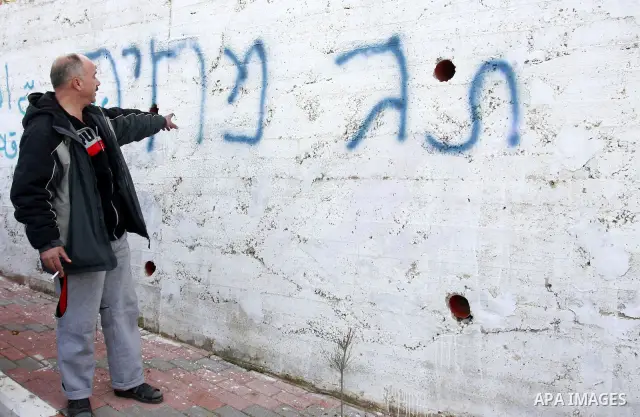 A Palestinian man stand next a graffiti in Hebrew which residents said was written by Jewish settlers in the West Bank Village of Harith near Nablus, Wednesday , Dec. 12, 2011. leaving behind a graffiti message in Hebrew...