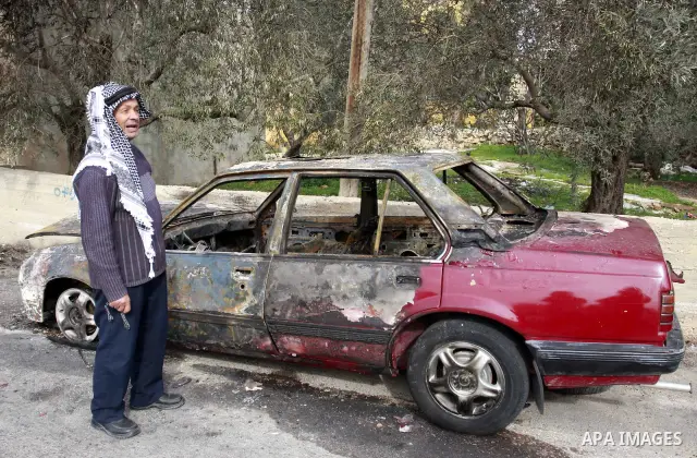 Palestinians stand next a burning vehicle which residents said was torched by Jewish settlers in the West Bank Village of Harith near Nablus, Wednesday , Dec. 12, 2011. leaving behind a graffiti message in Hebrew indicat...