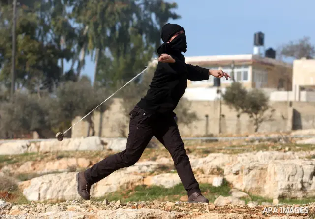 A Palestinian demonstrator uses a sling to hurl a stone towards Israeli security forces during clashes at a weekly protest against a nearby Jewish settlement, in the West Bank village of Nabi Saleh, near Ramallah Decembe...