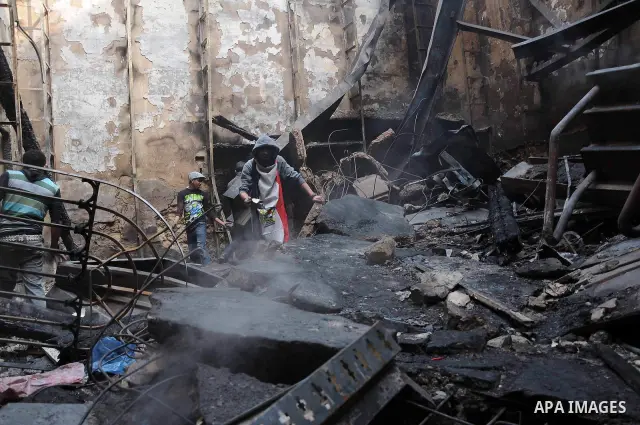 Smokes rises as an Egyptian protester helps extinguish smoldering valuable books and documents salvaged from the two story building of the Egyptian Scientific Complex after it was almost gutted by fire which broke out du...