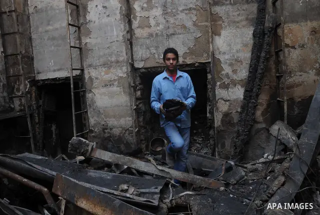 Smokes rises as an Egyptian protester helps extinguish smoldering valuable books and documents salvaged from the two story building of the Egyptian Scientific Complex after it was almost gutted by fire which broke out du...