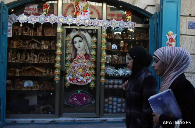Palestinian women walk front of shop to sell a nativity figurines are made in an olive wood factory in the West Bank town of Bethlehem, ahead of Christmas,Thursday, Dec. 22, 2011. Photo by Issam Rimawi Photo