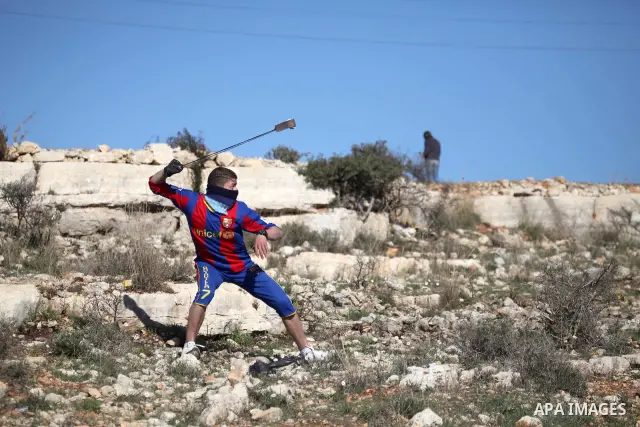 A Palestinian youth uses a sling to throw a stone toward Israeli soldiers during clashes at a weekly protest in the West Bank village of Nabi Saleh, near Ramallah, December 23, 2011.