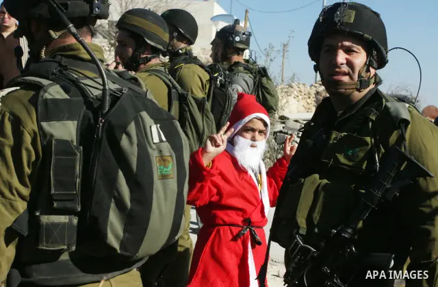 A young demonstrator dressed as Santa Claus stands near Israeli soldiers standing guard during a protest against the controversial Israeli barrier in the West Bank village of al-Masara near Bethlehem December 23, 2011. P...