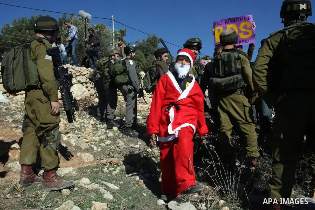 A young demonstrator dressed as Santa Claus stands near Israeli soldiers standing guard during a protest against the controversial Israeli barrier in the West Bank village of al-Masara near Bethlehem December 23, 2011. P...