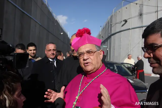 The Latin Patriarch of Jerusalem Fouad Twal (L) waves near the controversial Israeli barrier as he heads to the Church of the Nativity to attend Christmas celebrations in the West Bank town of Bethlehem December 24, 2011...