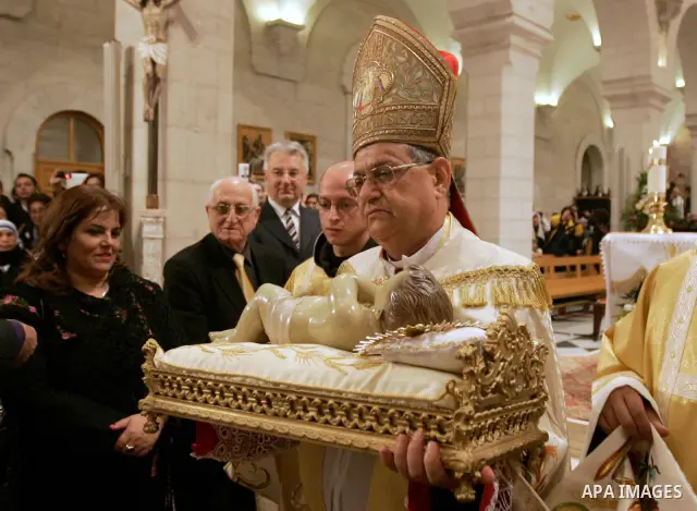 Latin Patriarch of Jerusalem Fouad Twal carries the statuette of baby Jesus during the Christmas midnight Mass at the Church of the Nativity, traditionally believed to be the birthplace of Jesus Christ, in the West Bank...