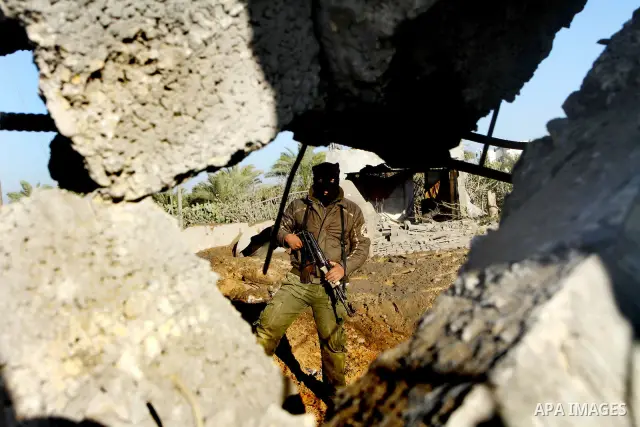 A masked Palestinian Islamic Jihad militant is seen through a tyre as he surveys the damage at a training camp after an Israeli air strike in Gaza December 29, 2011. The Israeli army confirmed that it targeted two sites...