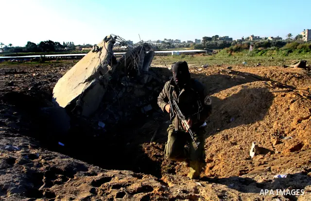 A masked Palestinian Islamic Jihad militant is seen through a tyre as he surveys the damage at a training camp after an Israeli air strike in Gaza December 29, 2011. The Israeli army confirmed that it targeted two sites...