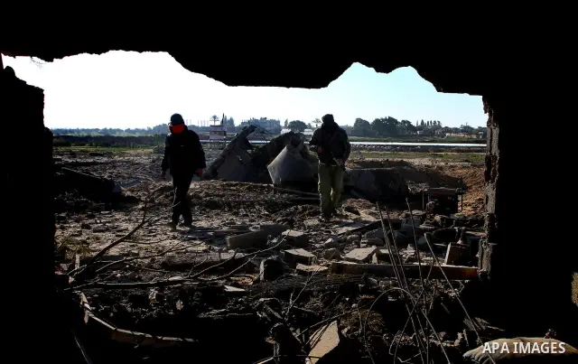 A masked Palestinian Islamic Jihad militant is seen through a tyre as he surveys the damage at a training camp after an Israeli air strike in Gaza December 29, 2011. The Israeli army confirmed that it targeted two sites...