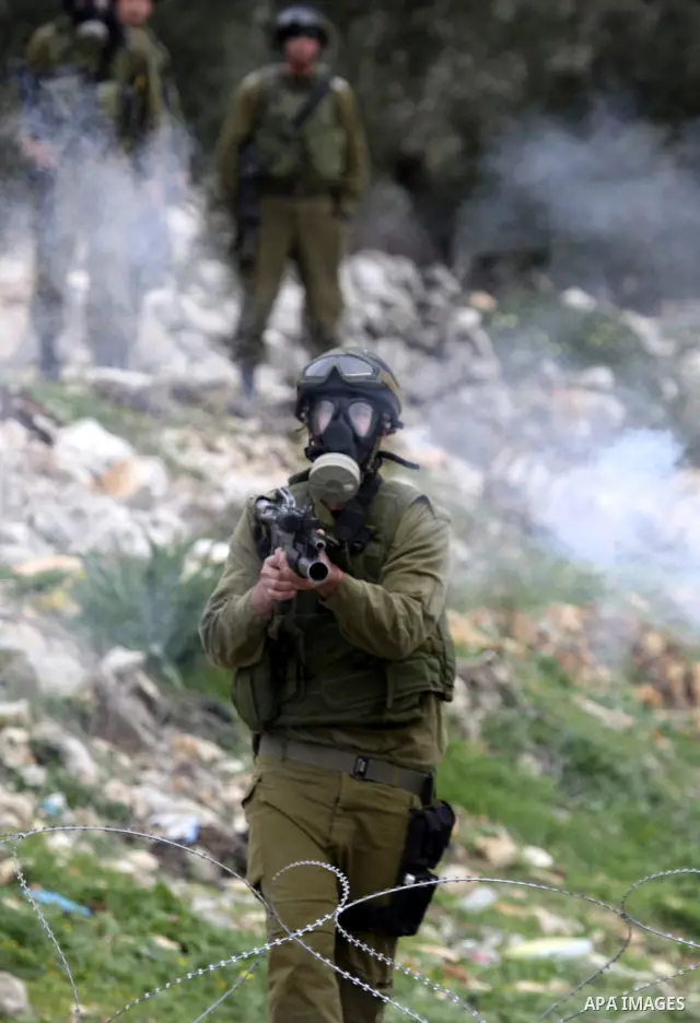 An Israeli soldier fires his weapon at Palestinian youths during a protest against the Jewish settlement of Qadomem, near the West Bank City of Nablus on 30 December 2011. Seven Palestinians were wounded during the clash...