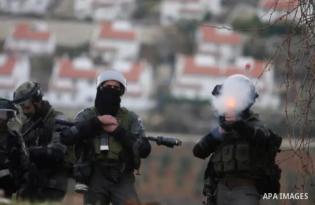 An Israeli soldier fires his weapon at Palestinian youths during demonstration against the expansion of the nearby Jewish settlement of Halamish in the West Bank village of Nabi Saleh near Ramallah, Friday, Dec. 30, 2011...