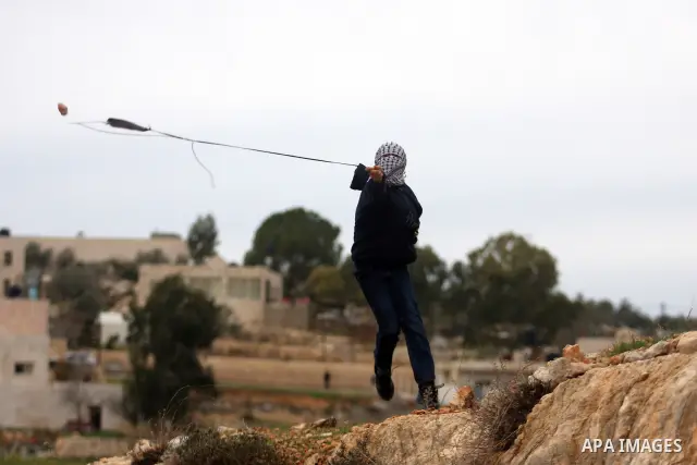 A Palestinian protester hurls stones at Israeli soldiers during demonstration against the expansion of the nearby Jewish settlement of Halamish in the West Bank village of Nabi Saleh near Ramallah, Friday, Dec. 30, 2011....