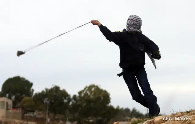 A Palestinian protester hurls stones at Israeli soldiers during demonstration against the expansion of the nearby Jewish settlement of Halamish in the West Bank village of Nabi Saleh near Ramallah, Friday, Dec. 30, 2011....