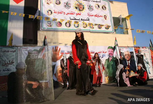 Palestinian folkloric dancers perform in front of a poster showing the late Palestinian leader Yasser Arafat during a celebration to to mark the 47th anniversary of the Fatah political movement. in the West Bank city of...