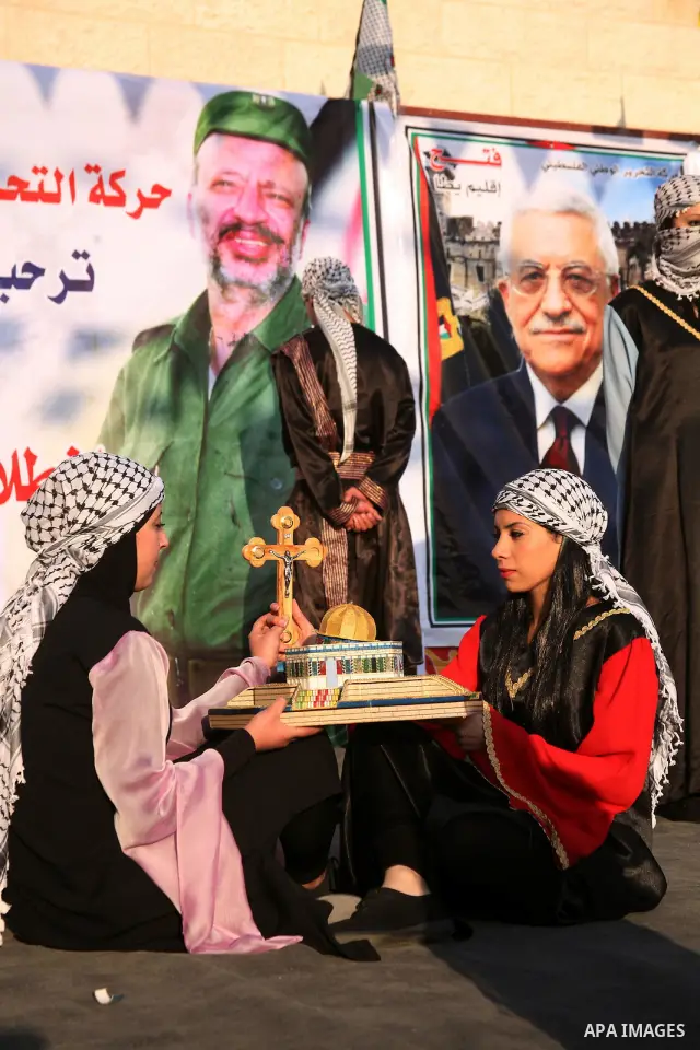 Palestinian folkloric dancers perform in front of a poster showing the late Palestinian leader Yasser Arafat during a celebration to to mark the 47th anniversary of the Fatah political movement. in the West Bank city of...
