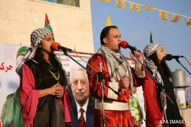 Palestinian folkloric dancers perform in front of a poster showing the late Palestinian leader Yasser Arafat during a celebration to to mark the 47th anniversary of the Fatah political movement. in the West Bank city of...