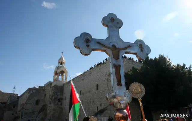 A Palestinian flag flutters next to a huge cross during a parade in Bethlehem's Manger Square outside the Church of the Nativity as Orthodox Christmas celebrations kicks off on 06 January 2012 in the traditional birthpla...