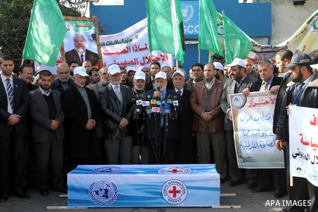 Palestinian Legislative Council members and other officials stand around a mock coffin covered with the emblems of the International Committee of the Red Cross (ICRC) and the United Nations Relief and Works Agency (UNRWA...