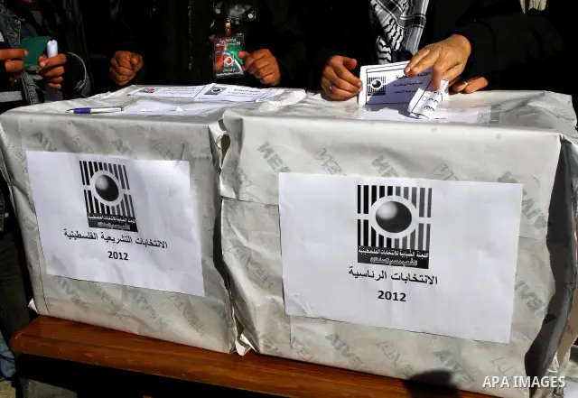 Palestinian activists wave Palestinian flags and hold election ballots during a protest calling for elections and unity between Fatah and Hamas during a demonstration in front of the recently reopened Central Elections c...