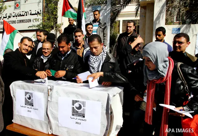 Palestinian activists wave Palestinian flags and hold election ballots during a protest calling for elections and unity between Fatah and Hamas during a demonstration in front of the recently reopened Central Elections c...