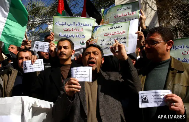 Palestinian activists wave Palestinian flags and hold election ballots during a protest calling for elections and unity between Fatah and Hamas during a demonstration in front of the recently reopened Central Elections c...