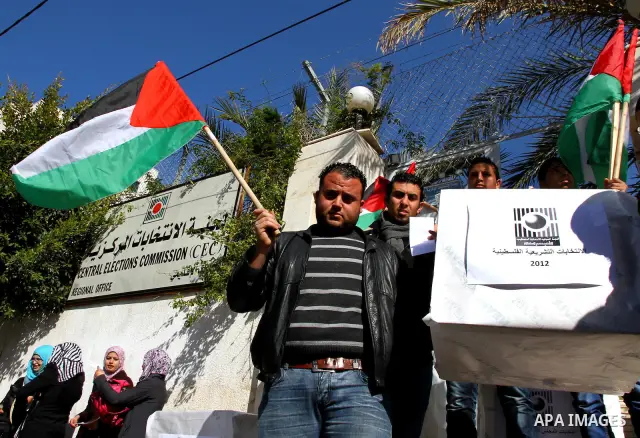 Palestinian activists wave Palestinian flags and hold election ballots during a protest calling for elections and unity between Fatah and Hamas during a demonstration in front of the recently reopened Central Elections c...