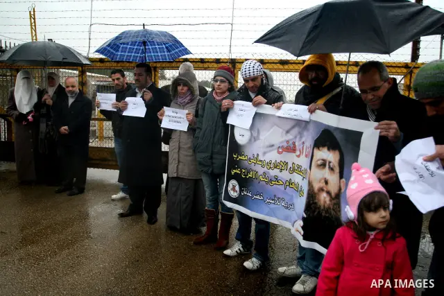 Maali (R), daughter of jailed Islamic Jihad spokesman Khodr Adnan (poster), stands with protesters holding signs against administrative detention during a demonstration outside Israel's Ofer prison near the West Bank tow...