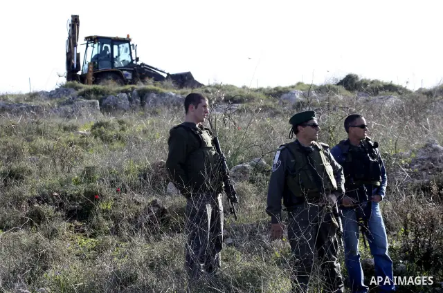 Israeli soldiers stand guards as a bulldozer of the Civil Administration during a demolition in the village of Kufr Qaddum near the Israeli settlement of Kdumim, in the northern West Bank, Sunday, Feb , 05, 2012. Photo b...