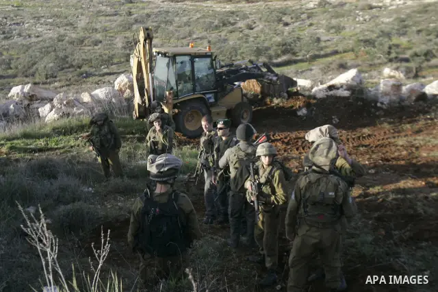 Israeli soldiers stand guards as a bulldozer of the Civil Administration during a demolition in the village of Kufr Qaddum near the Israeli settlement of Kdumim, in the northern West Bank, Sunday, Feb , 05, 2012. Photo b...