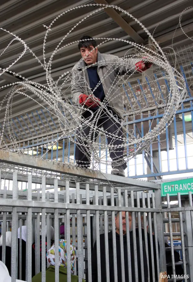 An Israeli worker rolls out razor over the heads of mainly Palestinians queuing between fencing to cross the Israeli army mained checkpoint in Qalandia, which lies between Jerusalem and the city of Ramallah, in the Israe...