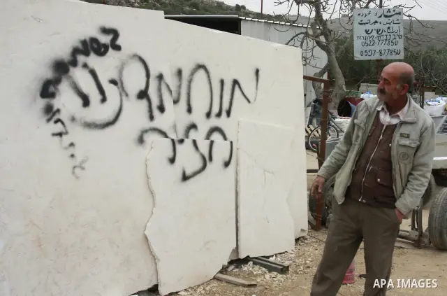 A Palestinian man looks at graffiti sprayed in the West Bank village near Nablus, Feb. 07, 2012. Palestinians say that Jewish extremists had been found on the streets of the village and the man fled, and two Jewish women...