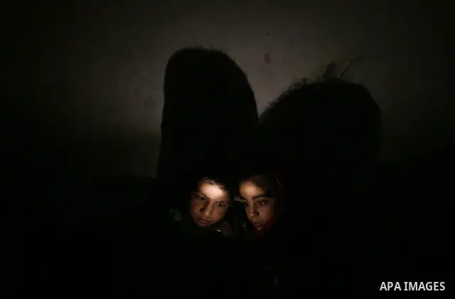 The display light of a mobile phone illuminates two Palestinian children playing games on the device at their familiy's home during an electricity power cut in the Jabaliya refugee refugee Gaza Strip, 07 February 2012. E...