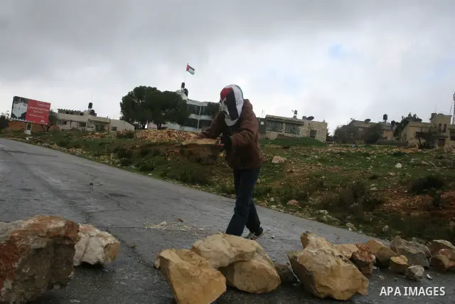 A Palestinian protester hurls stone at Israeli troops during a demonstration against the expansion of the nearby Jewish settlement of Halamish in the West Bank village of Nabi Saleh near Ramallah, Friday, Feb. 10, 2012....