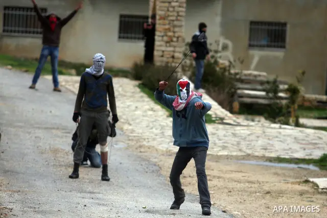 A Palestinian protester hurls stone at Israeli troops during a demonstration against the expansion of the nearby Jewish settlement of Halamish in the West Bank village of Nabi Saleh near Ramallah, Friday, Feb. 10, 2012....