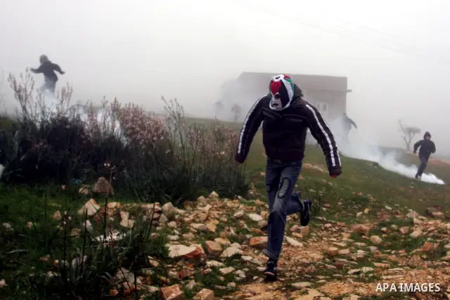 A Palestinian protester hurls stone at Israeli troops during a demonstration against the expansion of the nearby Jewish settlement of Halamish in the West Bank village of Nabi Saleh near Ramallah, Friday, Feb. 10, 2012....