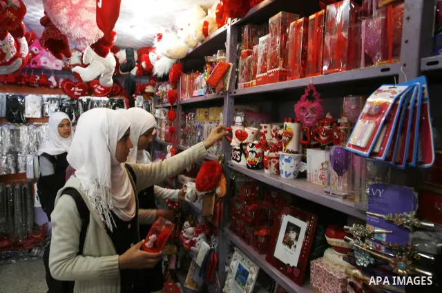 Palestinian girls are buying the hearts of love in the shop as they pass a display of hearts to commemorate Valentine's Day adorned with sayings about love, in Rafah, southern Gaza Strip on February 13, 2012. Valentine's...
