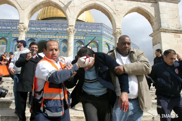 A Palestinian medic and a civilian assist a Palestinian man bleeding from his head as they remove him from near the Dome of the Rock, behind, during running clashes between Palestinians and Israeli policemen on the compo...