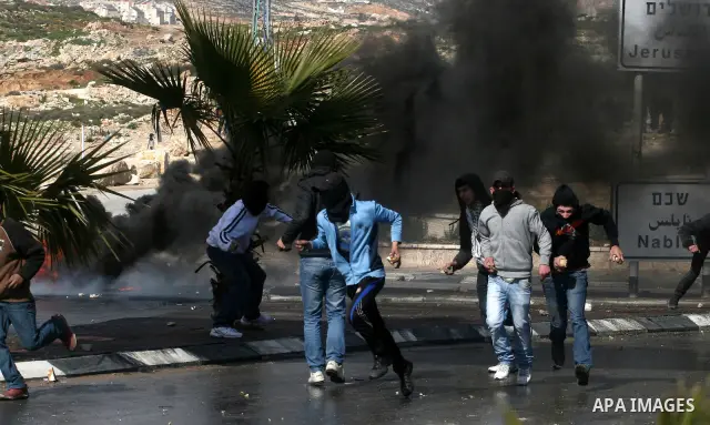 Masked Palestinian protesters run away from tear gas fired by Israeli security forces, not pictured, during clashes in the West Bank town of Al-Ram, near Jerusalem, Saturday, Feb. 25, 2012. Clashes erupted after the fune...