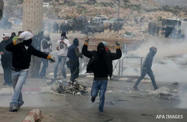 Masked Palestinian protesters run away from tear gas fired by Israeli security forces, not pictured, during clashes in the West Bank town of Al-Ram, near Jerusalem, Saturday, Feb. 25, 2012. Clashes erupted after the fune...