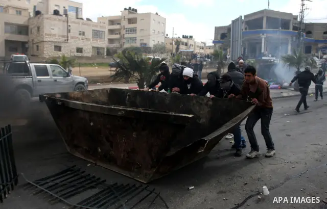 Masked Palestinian protesters run away from tear gas fired by Israeli security forces, not pictured, during clashes in the West Bank town of Al-Ram, near Jerusalem, Saturday, Feb. 25, 2012. Clashes erupted after the fune...