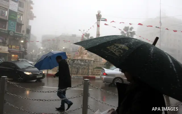 Palestinians walk in a street during the heavy rain and cold winds in the West Bank city of Ramallah on 29 Feb, 2012. Photo by Issam Rimawi