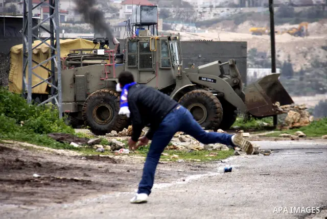 A Palestinian protester throws stones at Israeli bulldozer during a demonstration against the expropriation of Palestinian land by Israel in the village of Kfar Qaddum, near the West Bank city of Nablus, on March 2, 2012...